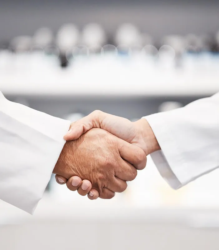 Two people in lab coats shaking hands