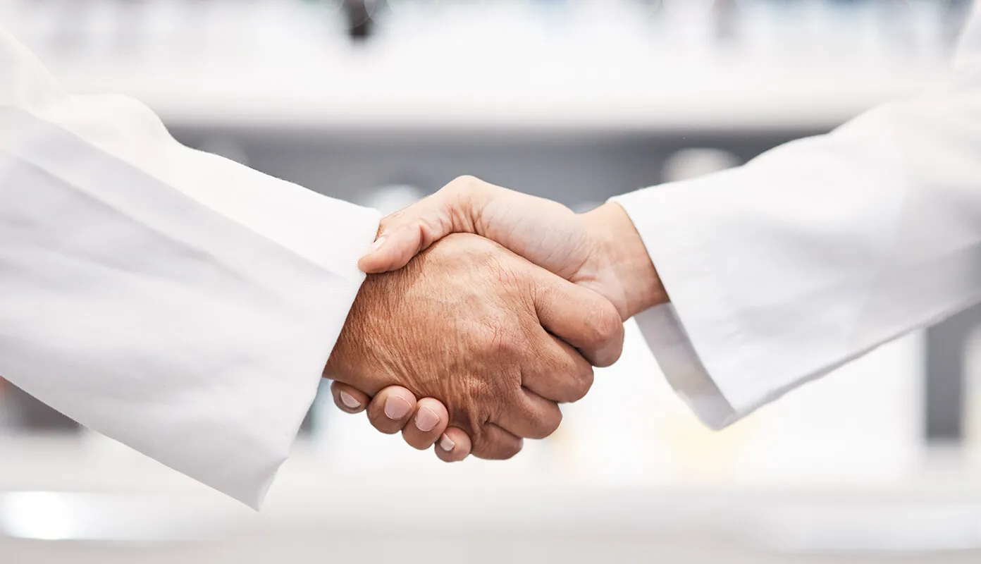 Two people in lab coats shaking hands